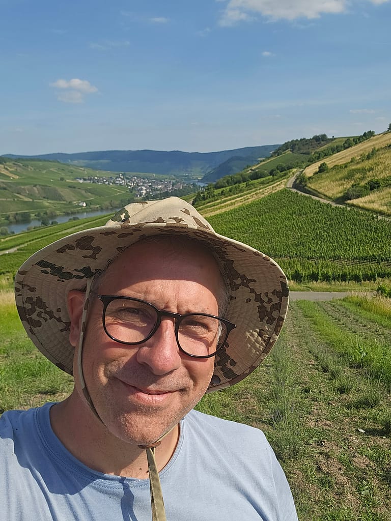 Mann mit Sonnenhut und Brille lächelt in die Kamera – im Hintergrund ein Lavendelfeld in Hanglage an der Mosel. Mario Kohlmann, Gründer von LAVELAL.
